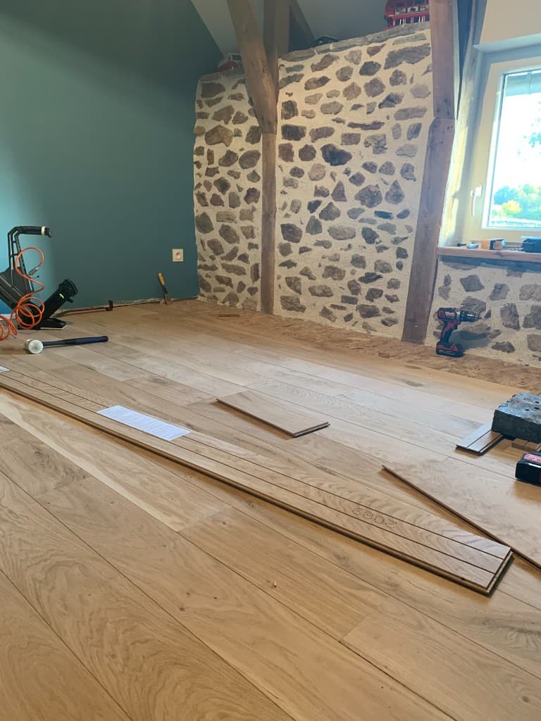 Hardwood planks being laid beside a stone wall during a custom floor installation